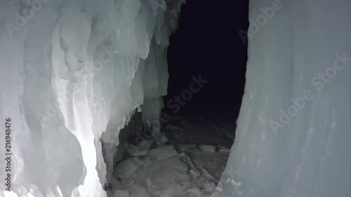 Travel woman on ice cave of Lake Baikal. Pov view selfie. Girl backpacker is walking of ice grot. Traveler looks at beautiful ice grotto. Hiker wears sports glasses, silver jacket, backpack, led lamp photo