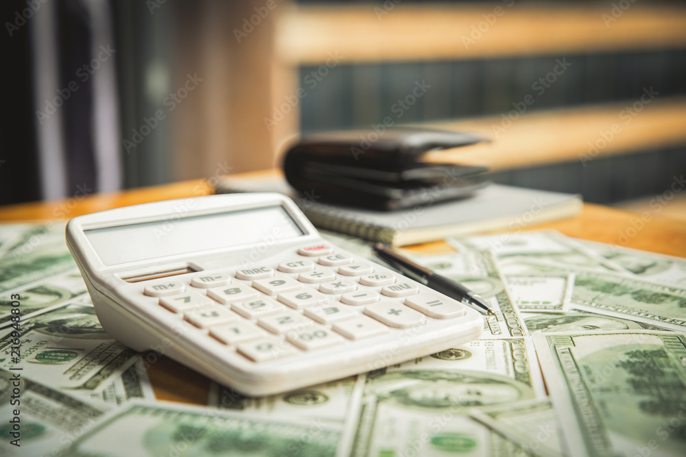 calculator pen wallet notebook placed on a banknote on a wooden table. calculator pen wallet notebook placed on a banknote on a wooden table.