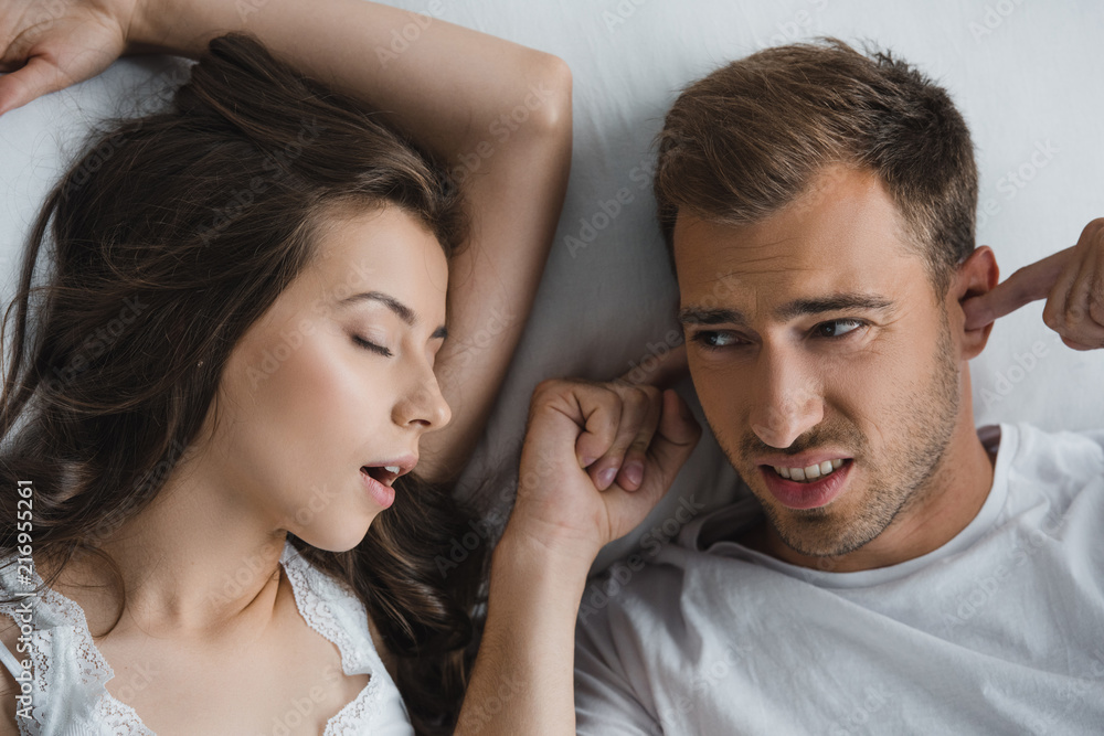 top view of man closing ears and looking at snoring wife in bed top view of man closing ears and looking at snoring wife in bed