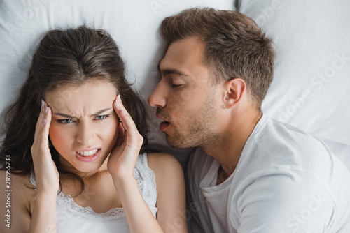 Foto young angry woman having headache while lying with snoring husband in bed