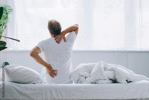 back view of man sitting on bed and suffering from back pain