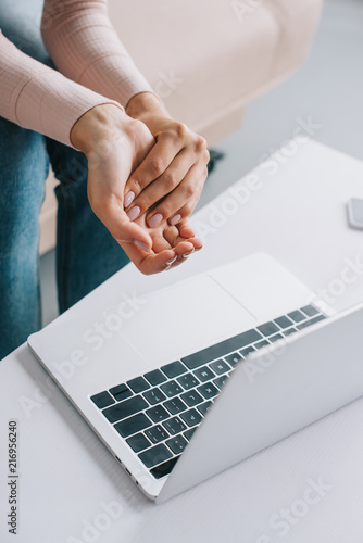 cropped shot of woman suffering from pain in hand while using laptop