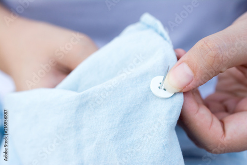 Hands of a woman sew a button with a needle close up. Woman is sewing buttons a shirt.