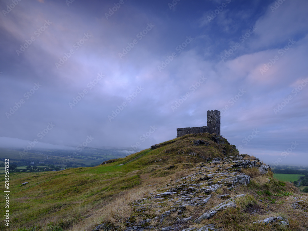 Summer sunrise on Brentor showning St Michael's church atop the tor with dramatic weather clouds of showers and mist, on the western edge of the Dartmoor National Park. UK