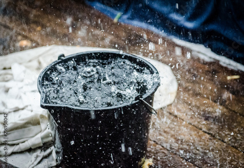 Rainy weather on the terrace in summer. The rain falls into the bucket and creates splashes.