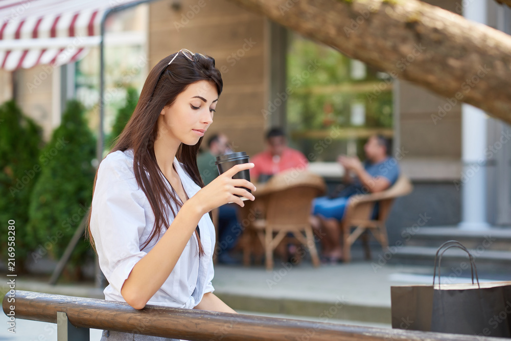 Young pretty student looking on paper cup with coffee, sitting on wooden bench. Young pretty student looking on paper cup with coffee, sitting on wooden bench.