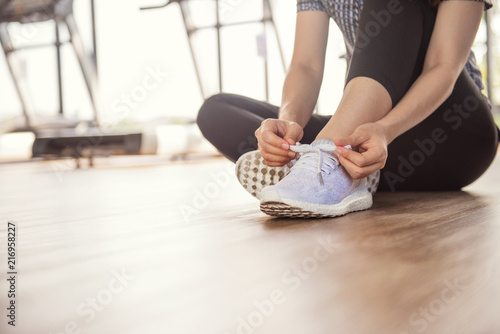 Woman tying running shoes on black floor background in gym fitness with sunlight. copy space.