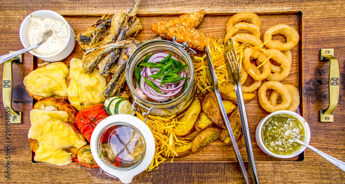 A fishing mix for a big company. Smoked mackerel, crispy salad, stuffed with mackerel deruny, fish sticks, onion rings, slices of potatoes, garlic and ginger sauces. On wooden pylony with two handles. photo