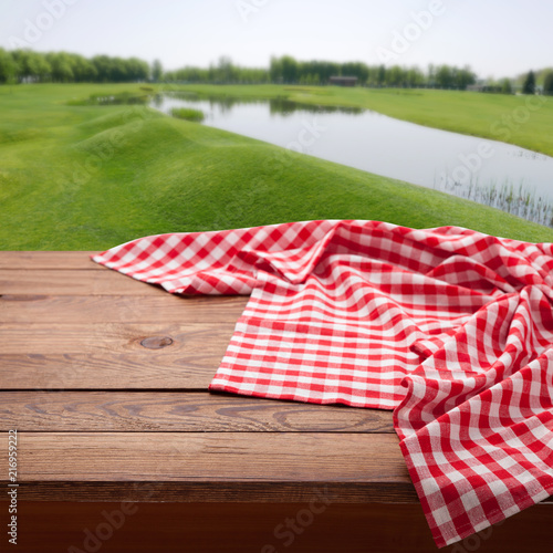 Red checkered tablecloth on wooden table. Napkin close up top view mock up. Summer rustic background.