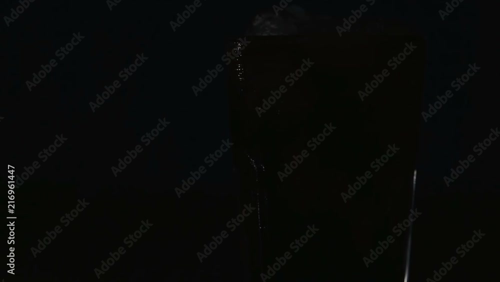 Cola with ice cubes and bubbles in glass, close-up, light moving. Cola drink, light in the dark. Cola with ice cubes and bubbles in glass, close-up, light moving. Cola drink, light in the dark.