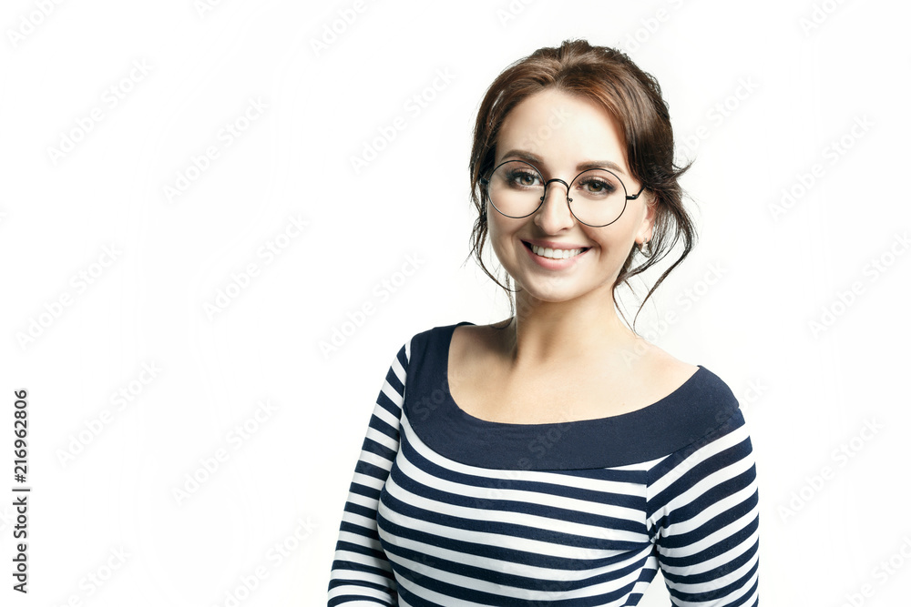 A young beautiful woman in a striped tight blouse and in round glasses widely smiles white teeth. Isolated on white background A young beautiful woman in a striped tight blouse and in round glasses widely smiles white teeth. Isolated on white background