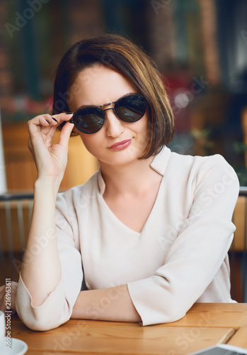 Canvastavla Young woman drinks coffee in cafeteria and posing with sunglasses