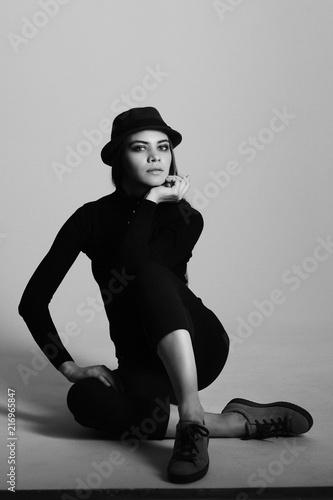 girl in a black suit with a hat, hair posing in the Studio on a gray background. black and white photo