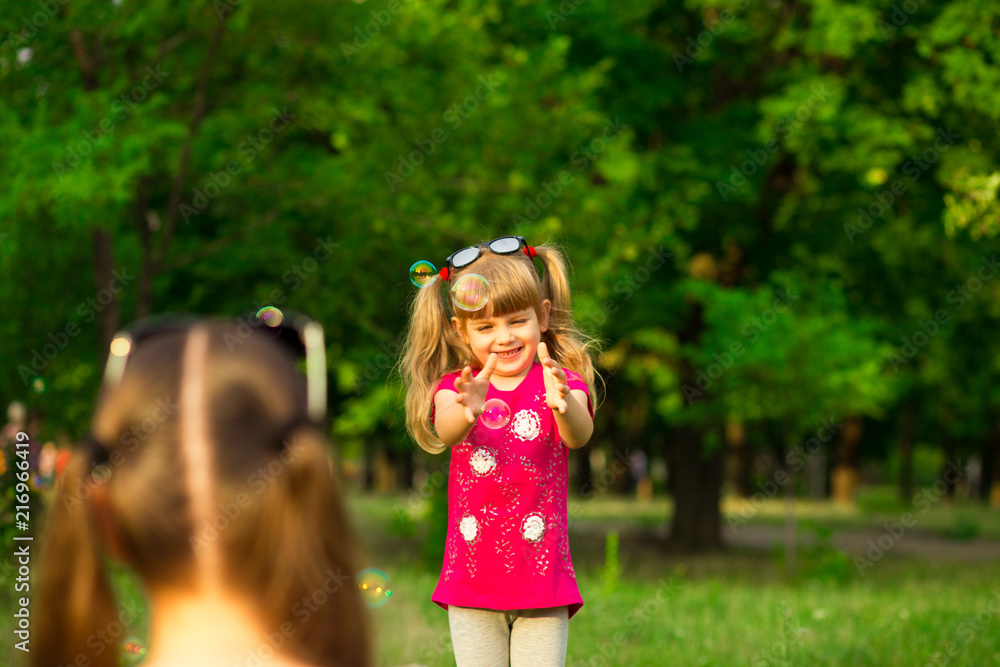 Young mother and little daughter playing in park with soap bubbles. Love family, parenthood, childhood Young mother and little daughter playing in park with soap bubbles. Love family, parenthood, childhood
