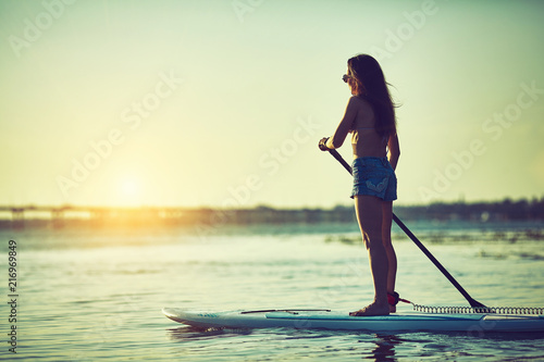 SUP Stand up Surf girl with paddle at sunset photo
