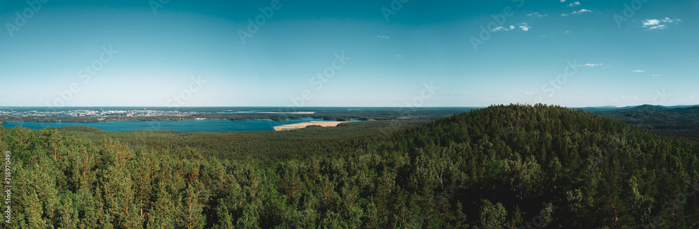 Aerial drone panoramic view of mountain peak with thin high tree trunks, mixed forest of birches and pine trees, lakes on the background, mountain Sugoyak, South Ural, Russia