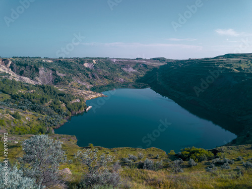 Aerial drone view of abandoned quarry with lake appeared on the bottom, the mirror surface of the water in the sunny evening, overgrown with forest shore, Ural, Russia