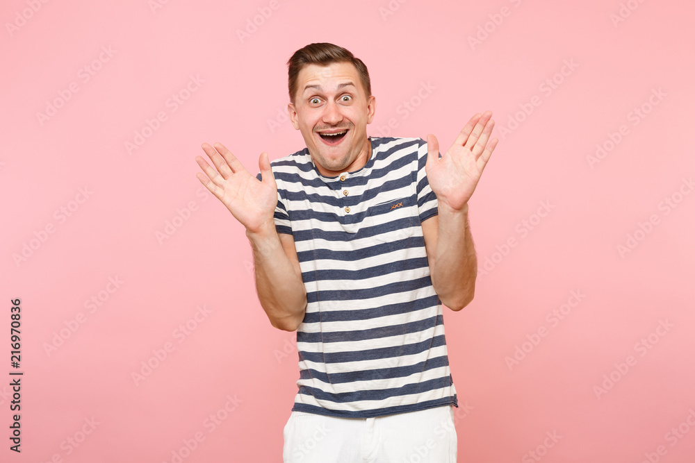 Fototapeta premium Portrait of cheerful surprised young hipster man dresssed casually in striped t-shirt spreading hands isolated on trending pink background. People sincere emotions, youth lifestyle concept. Copy space