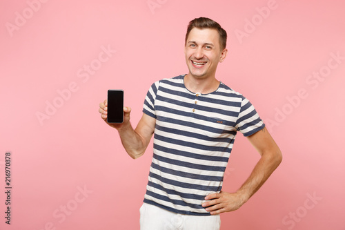 Portrait of man in striped t-shirt showing mobile phone camera with blank black empty screen copy space isolated on trending pastel pink background. People sincere emotions concept. Advertising area. © ViDi Studio