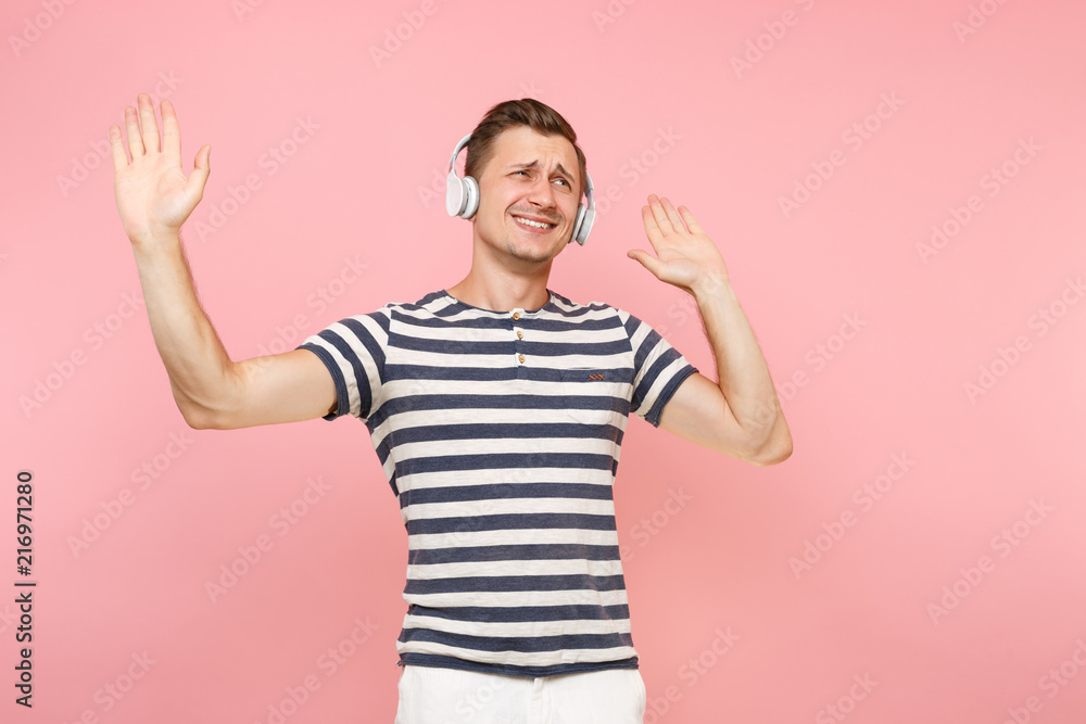 Portrait of smiling young man wearing striped t-shirt listening to music with white wireless headphones, enjoy isolated on trending pastel pink background. People sincere emotions lifestyle concept. Portrait of smiling young man wearing striped t-shirt listening to music with white wireless headphones, enjoy isolated on trending pastel pink background. People sincere emotions lifestyle concept.