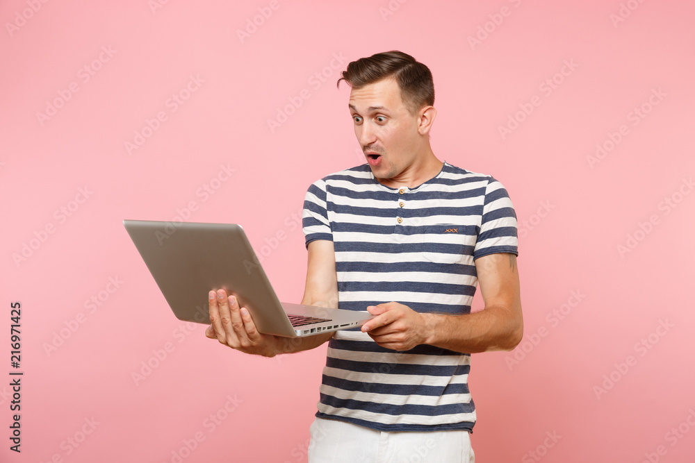 Portrait of handsome young man wearing striped t-shirt working on laptop computer, copy space isolated on trending pastel pink background. People sincere emotions lifestyle concept. Advertising area. Portrait of handsome young man wearing striped t-shirt working on laptop computer, copy space isolated on trending pastel pink background. People sincere emotions lifestyle concept. Advertising area.