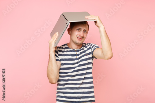 Portrait of handsome young man in striped t-shirt hold above head laptop computer, copy space isolated on trending pastel pink background. People sincere emotions lifestyle concept. Advertising area.