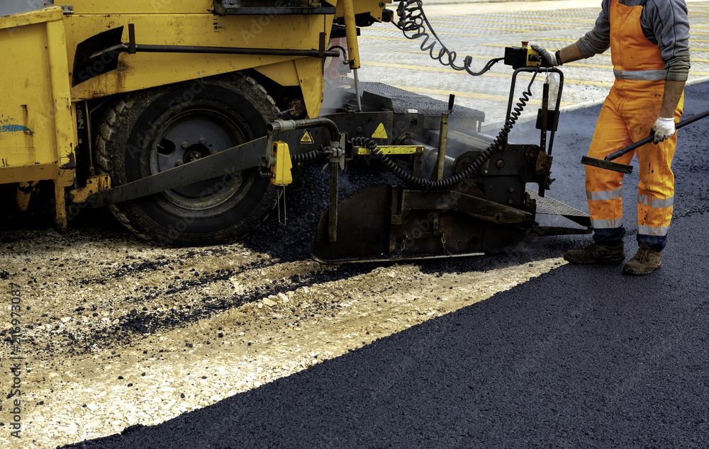 Workers regulate tracked paver laying asphalt heated to temperatures above 160 ° pavement on a runway Workers regulate tracked paver laying asphalt heated to temperatures above 160 ° pavement on a runway
