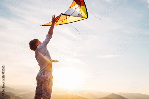 Boy jumps and strats to fly a kite in the sky photo