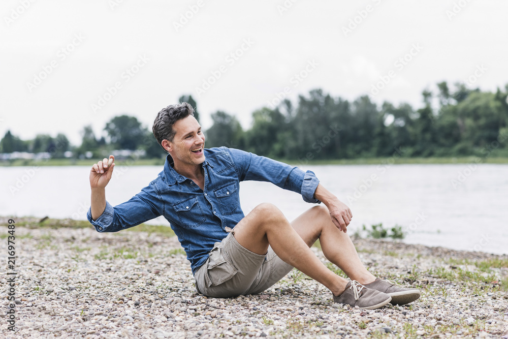 Laughing man sitting at the riverside throwing stones Laughing man sitting at the riverside throwing stones