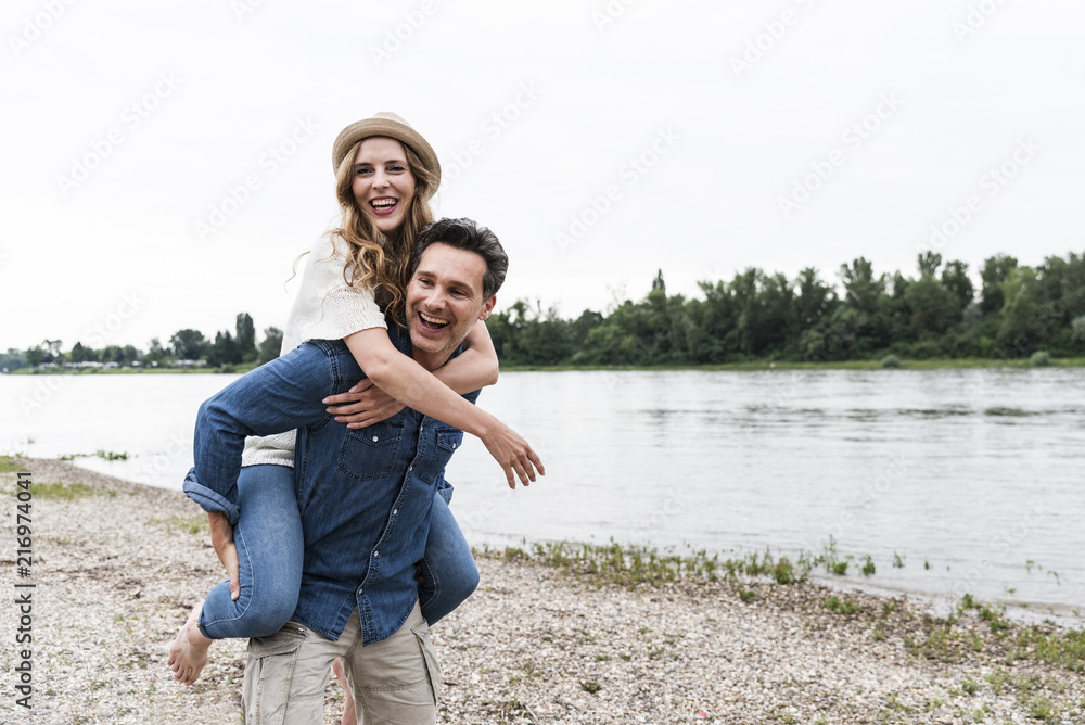 Happy man carrying girlfriend piggyback at the riverside Happy man carrying girlfriend piggyback at the riverside