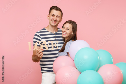 Portrait of couple hold wooden word letters love. Woman and man in blue clothes celebrating birthday holiday party on pastel pink background with colorful air balloons. People sincere emotions concept