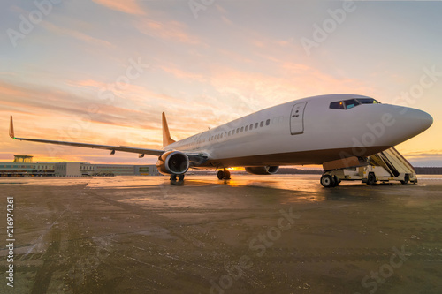Passenger airplane parked at the airport. Commercial jet plane with sunset sky background, standing at the airport and waits for departure.