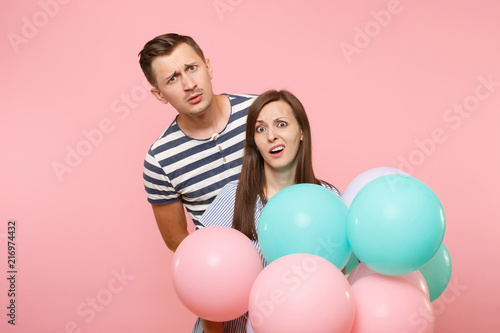 Portrait of young fun crazy mad couple in love. Woman and man in blue clothes celebrating birthday holiday party on pastel pink background with colorful air balloons. People sincere emotions concept.