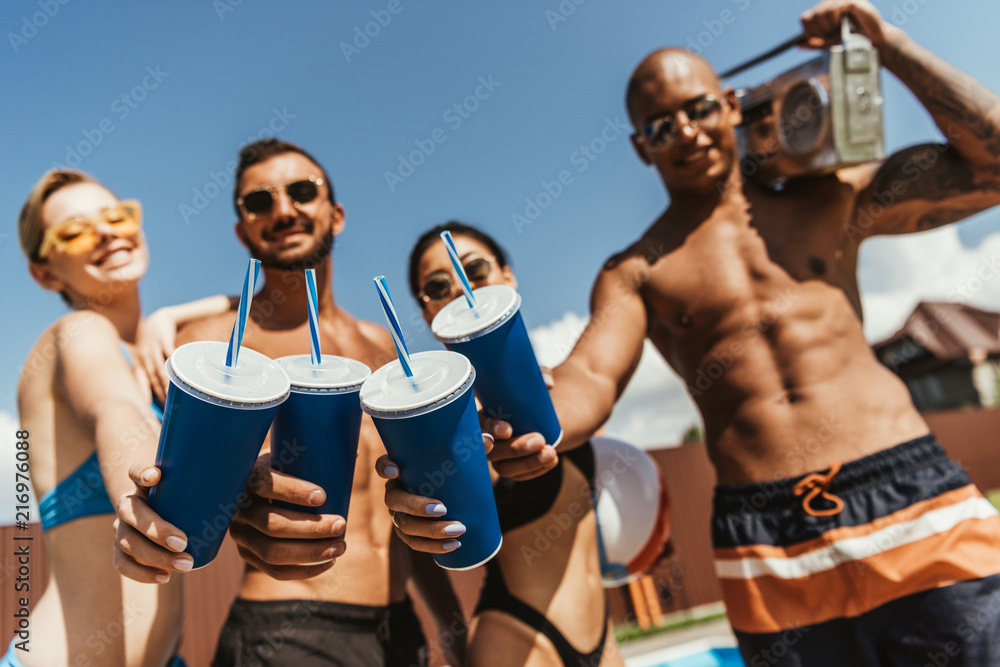multicultural friends with clinking cups and holding retro boombox, selective focus multicultural friends with clinking cups and holding retro boombox, selective focus
