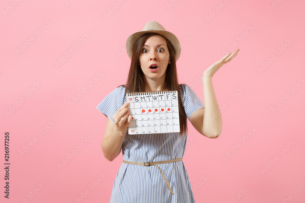 Portrait of shocked woman in blue dress, hat holding periods calendar for checking menstruation days isolated on bright trending pink background. Medical, healthcare, gynecological concept. Copy space Portrait of shocked woman in blue dress, hat holding periods calendar for checking menstruation days isolated on bright trending pink background. Medical, healthcare, gynecological concept. Copy space