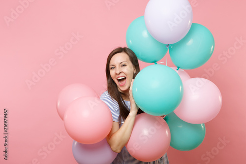 Portrait of joyful young happy woman with opened mouth in blue dress holding colorful air balloons isolated on bright trending pink background. Birthday holiday party, people sincere emotions concept.