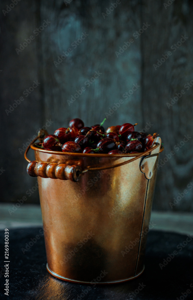 Yellow brass bucket with berry of red gooseberry stand on black stone stand  on stone stand on vintage wood background Stock Photo