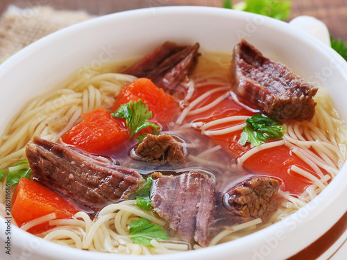 Beef soup with noodles and vegetables in soup bowl closeup photo