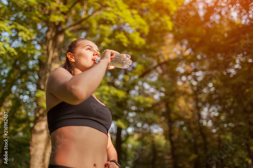 Young sportive woman drinking water after workout in summer park. Healthy way of life. Importance of water