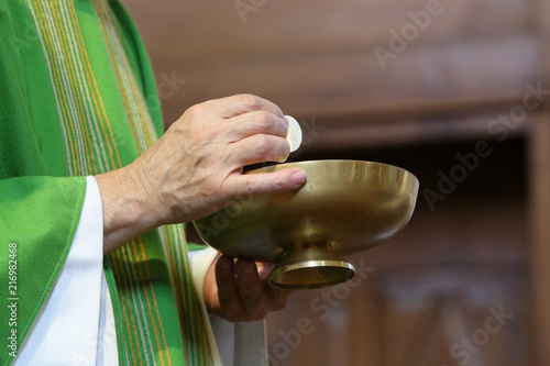 Prêtre tenant une hostie au-dessus d'une patène. Donner la communion. / Hostie and paten. Give communion.