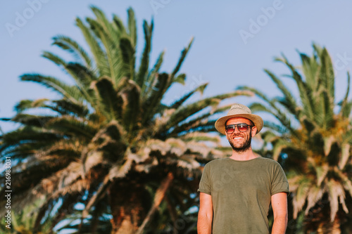 Young man standing by the palm trees looking at sun