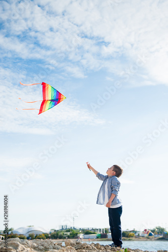 happy caucasian little kid playing with flying kite near sea shore at summer sunset