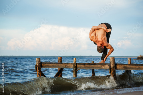 Young yoga trainer practicing janushirshasana pose on a wooden pier on a sea shore.