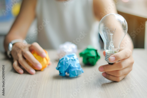 Business woman Hand holding light bulb or lamp with colorful crumpled paper on wooden table. New Idea  Creative  Genius and Innovation concepts