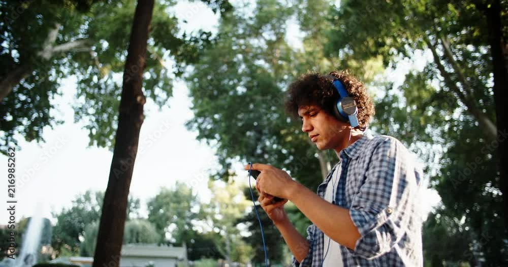 Young asian man walking down the street, using smartphone listening to music in headphones - closeup 4k
