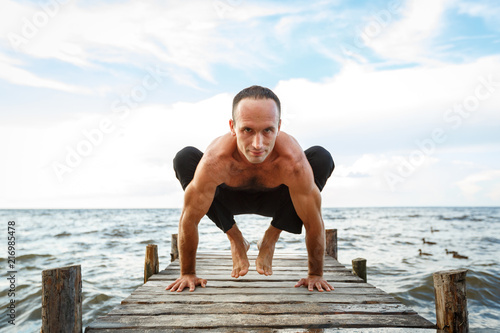 Young yoga trainer practicing yoga exercises on a wooden pier on a sea or river shore