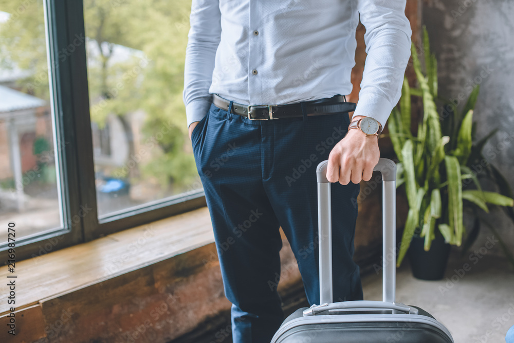 cropped image of businessman with hand in pocket standing with suitcase at home cropped image of businessman with hand in pocket standing with suitcase at home
