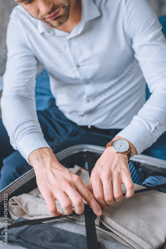 selective focus of businessman with wristwatch packing luggage in suitcase