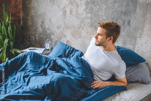 confident young man waking up in his bed during morning time at home