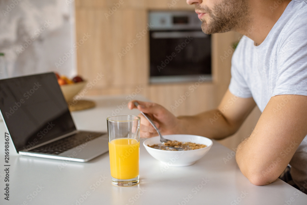 cropped image of man eating flakes at kitchen table with fresh juice and laptop cropped image of man eating flakes at kitchen table with fresh juice and laptop